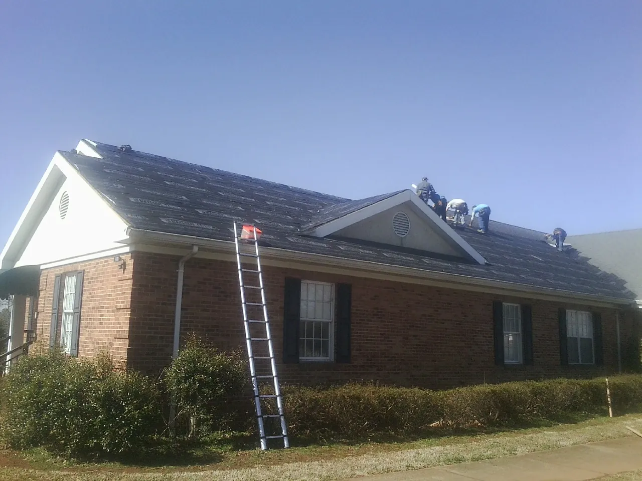 Crew tearing shingles off a brick ranch roof with a ladder set — Emergency Roof Repair work by our crew in Denton