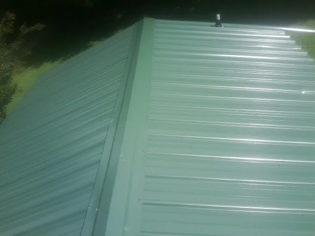 New green metal panels meeting at the ridge of a roof — Flat Roof Repair work by our crew in Denton