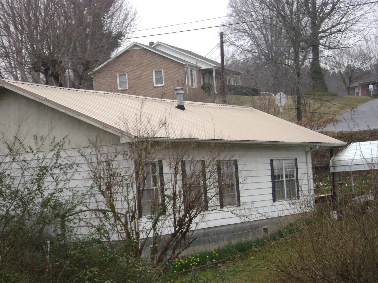 Tan metal roof on a white sided house set into a hillside — Commercial Roofing by Roofing Brothers in Denton